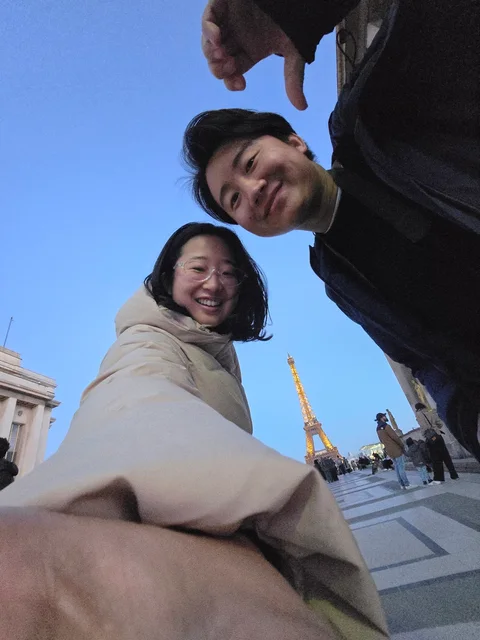 Nam-Hee and Hiroo taking a selfie with the Eiffel Tower behind them.