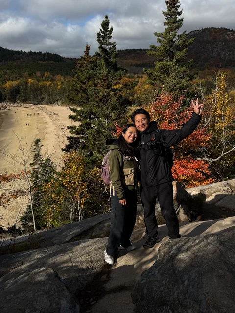 Nam-Hee and Hiroo posing on a rocky overlook among autumn trees.
